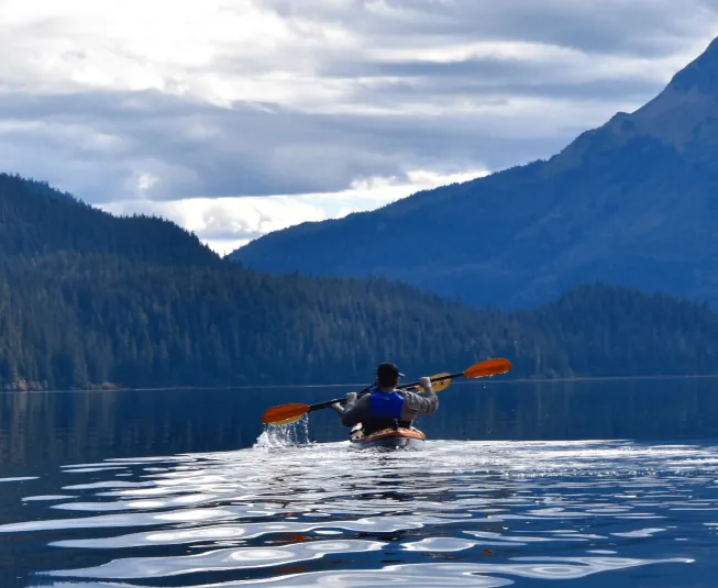 Kayaker paddling across an Alaska mountain lake