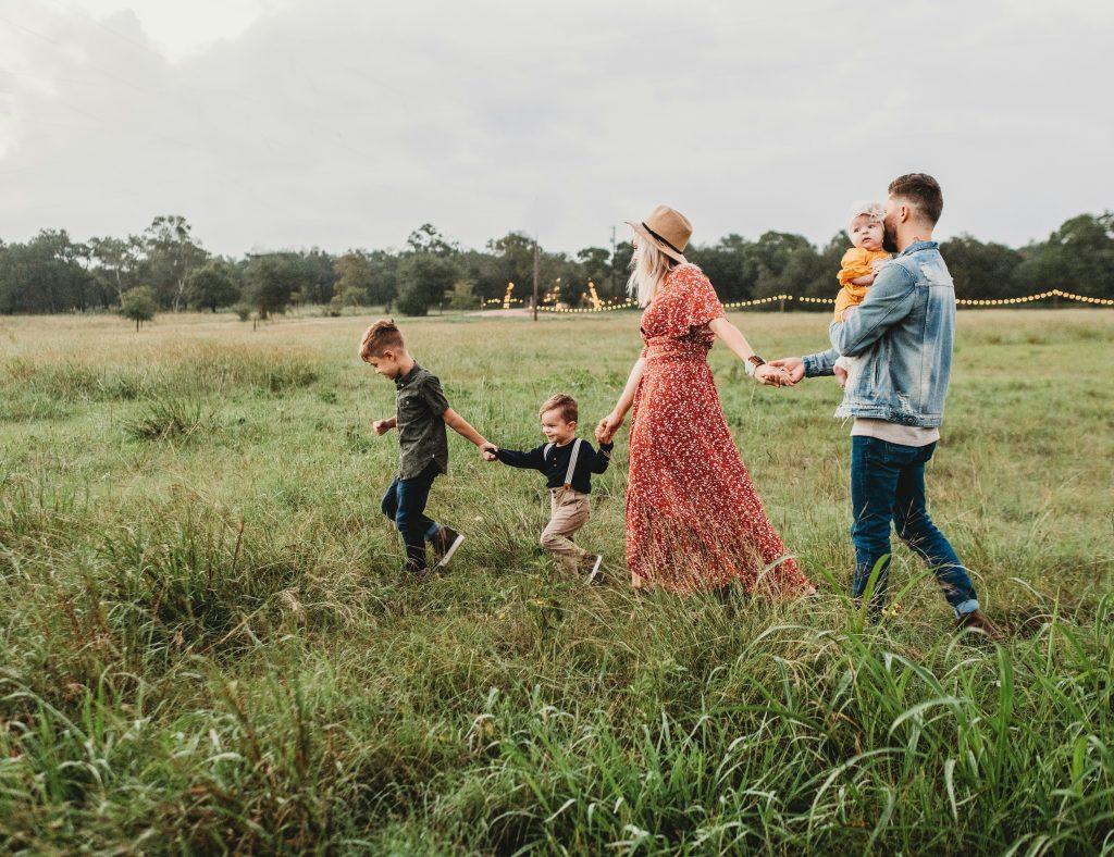 Family holding hands and walking through a grassy field
